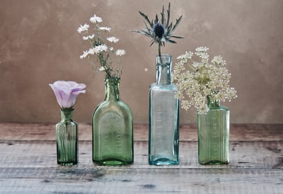 Three green and a blue glass vase, there are flowers inside
